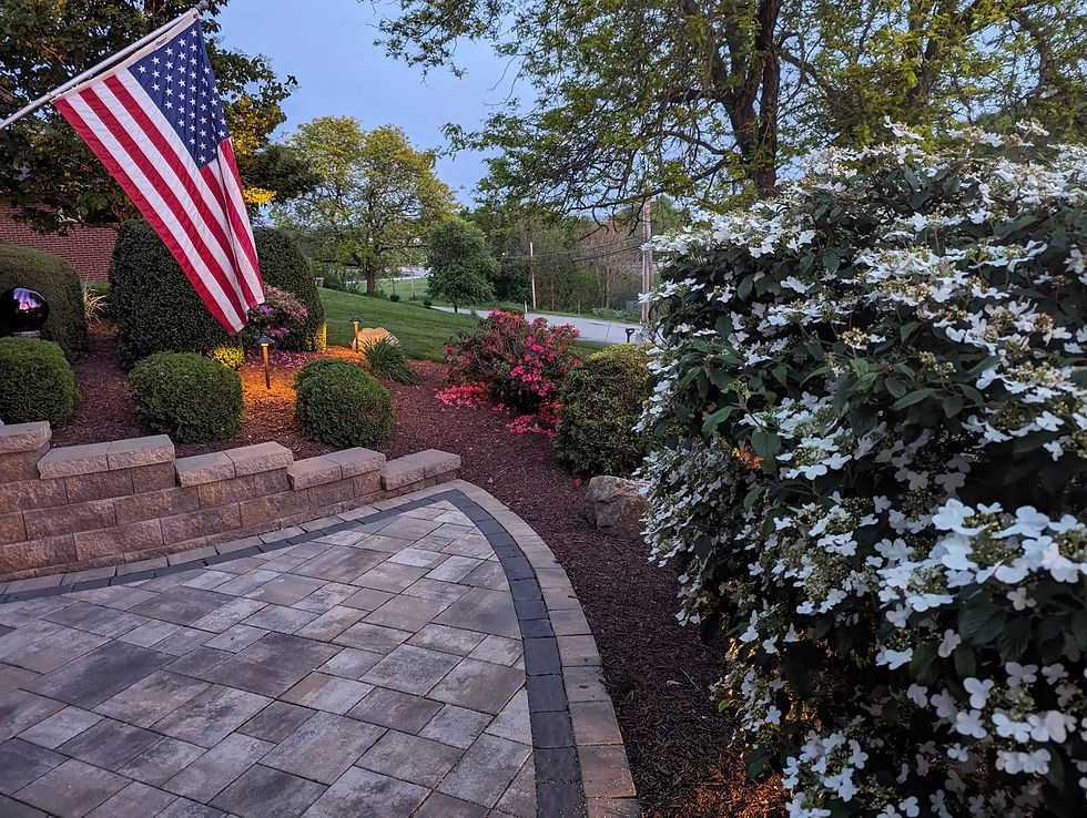 Paver patio with landscape lighting and American flag in Mount Pleasant, PA by Skowronek Landscaping & Excavating.