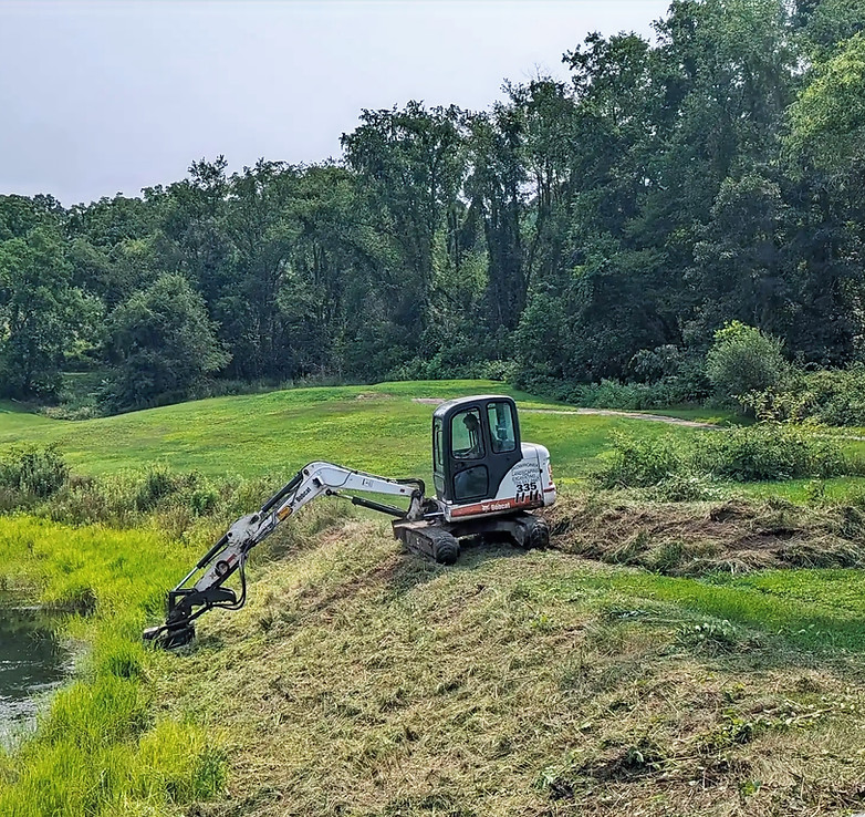 Mini excavator clearing brush and reshaping pond bank in Irwin, PA, land clearing by Skowronek Landscaping & Excavating.