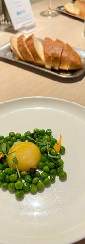 Poached Egg yolk with surrounded by green peas, microgreens, and caviar. Served with bread to be eaten as a spread.