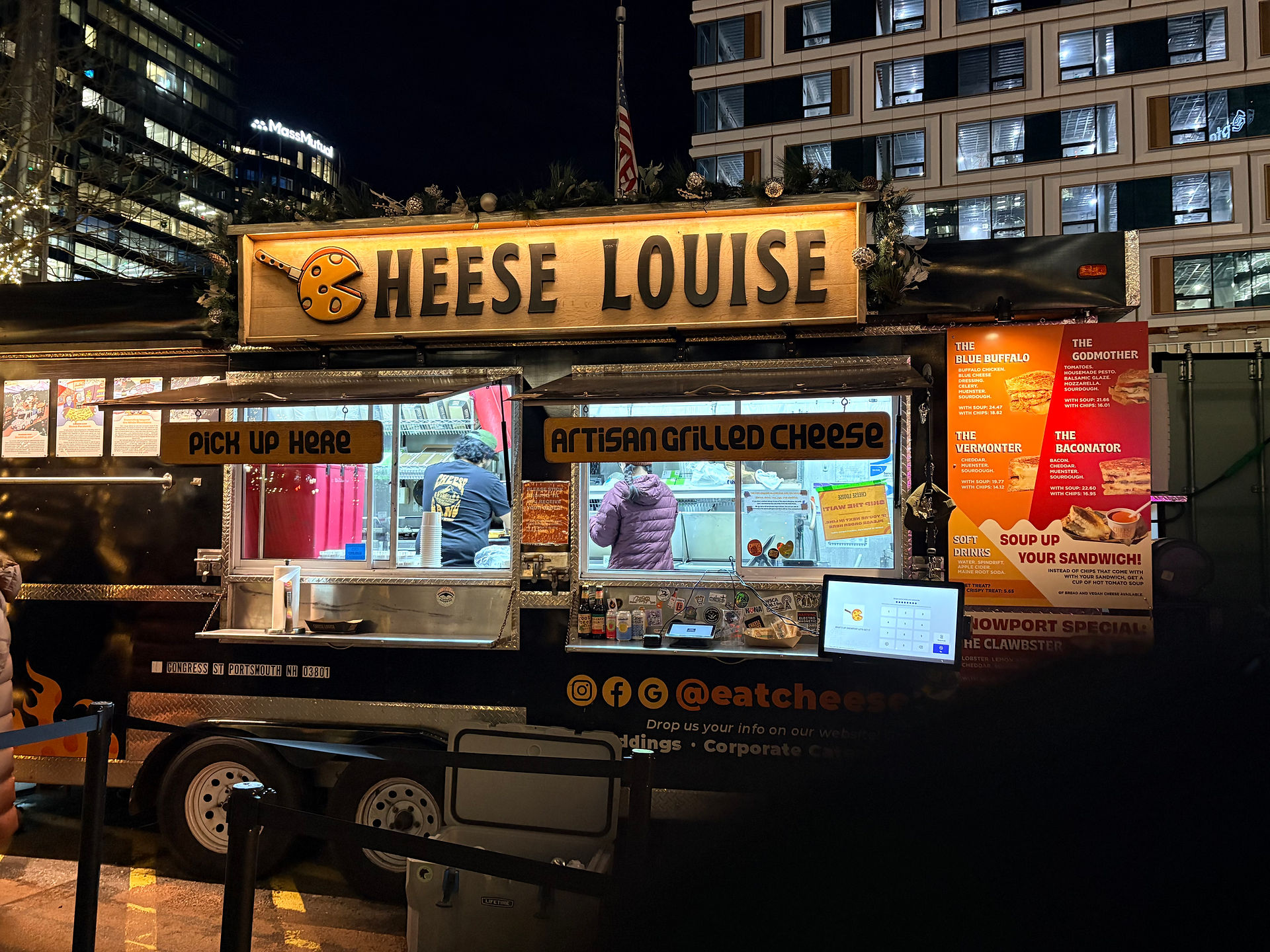 Black and yellow Cheese Louise Food track with yellow sign at the top with the business name in black lettering. A menu is on the right side of the truck.