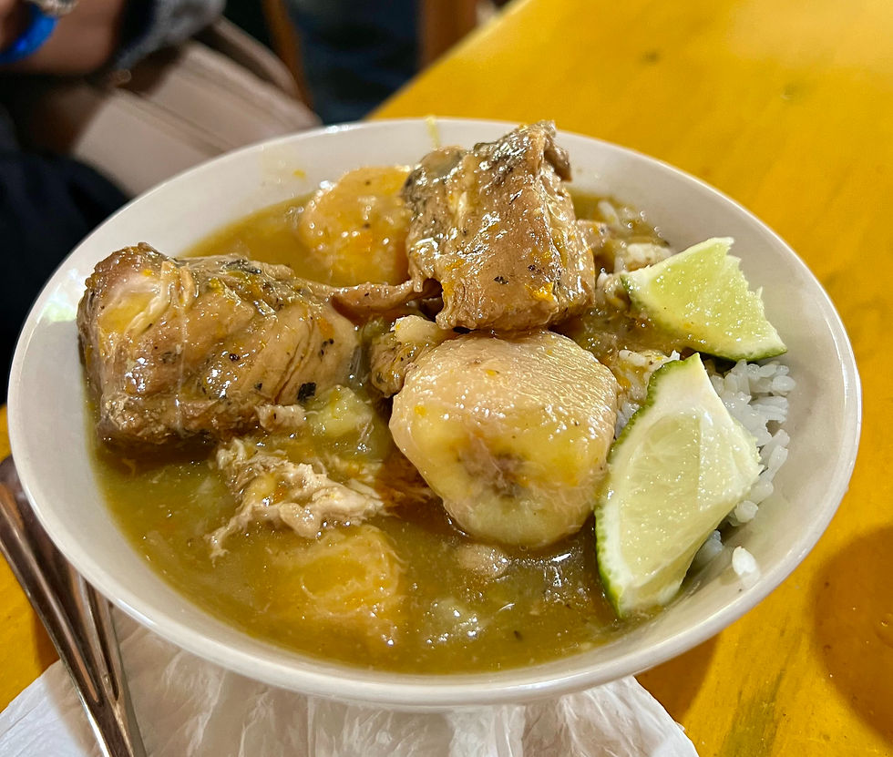 Bowl of sancocho with meat, plantains, lime wedges, and rice on a wooden table. Warm colors create a cozy, inviting atmosphere.