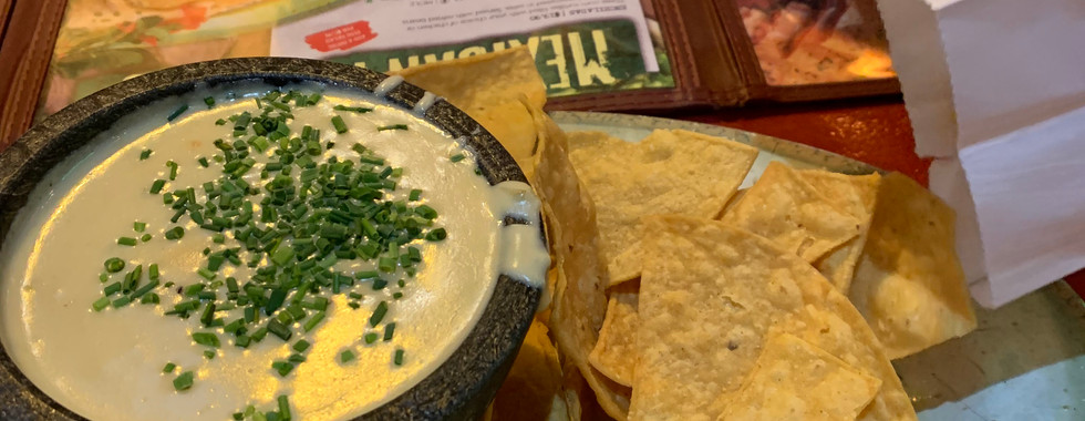 Queso dip topped with chives on the left with fresh corn tortilla chips on the right side.