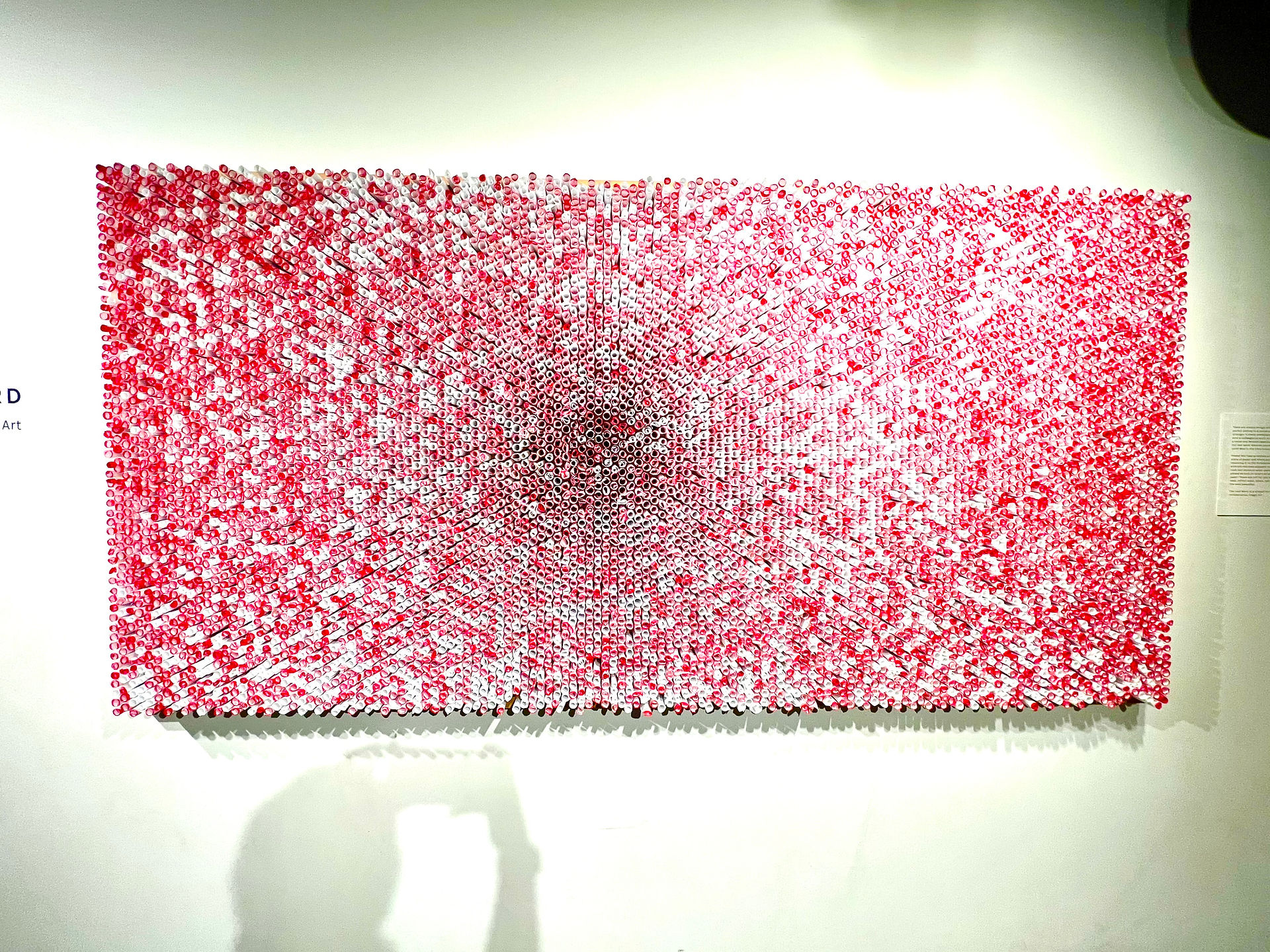 The Last Word by Illegal Art full image of the artwork. A honeycomb structure fastened to the wall filled with miniature scrolls of paper. Paper with the white ends facing out are blank and participants can write on them. Scrolls with red facing outward have been written by previous participants and can be read by others.