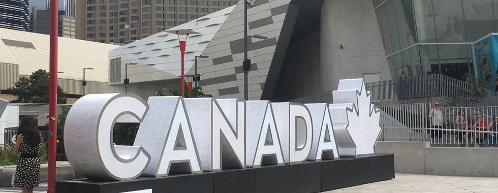 White large letters to spell Canada with a matching maple leaf in a long horizontal structure, perfect for taking pictures at the space outside Ripley's Aquarium, the CN Tower, and Rogers Centre.