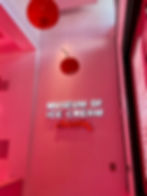 Museum of Ice Cream in 3D white letters that are backlit with Austin underneath in red. The walls is pink and there are large maraschino cherries hanging from the ceiling.