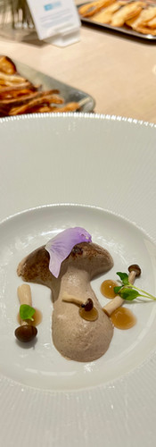 Mushroom paté in plated to look like a cap mushroom with a flower on top and small mushrooms sprinkled on top. Serviced with toasted sourdough bread.