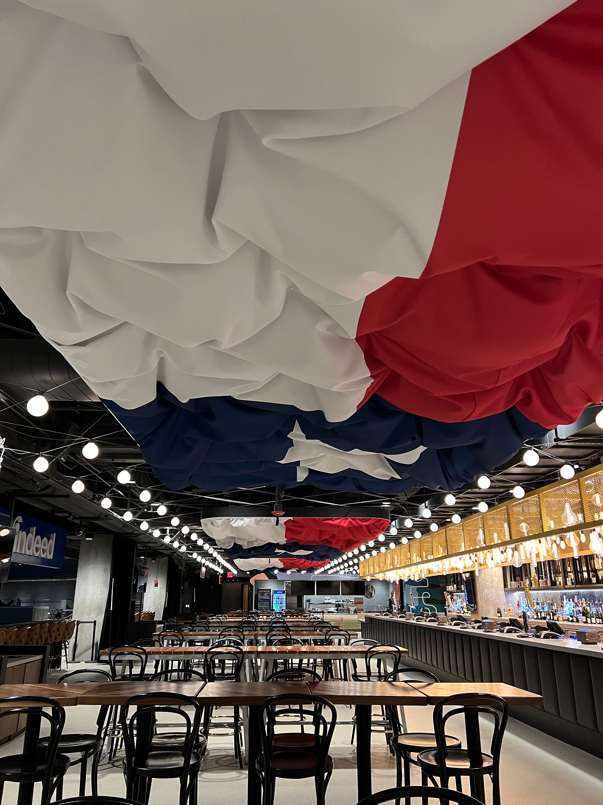 Indeed Lounge featuring a bar on the right, bar seating throughout the middle of the lounge, and large Texas flags across the ceiling