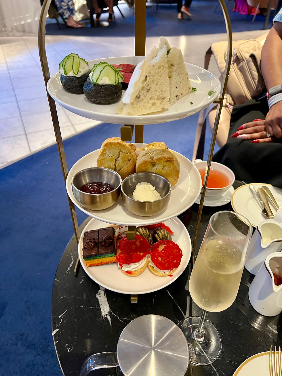 Afternoon tea set with sandwiches, pastries, scones, and spreads on a tiered stand. Glass of champagne on a black marble table.