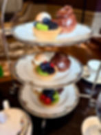 Three-tiered dessert stand with tarts and chocolate pastries. Elegant plates, warm dining room setting, cozy mood.