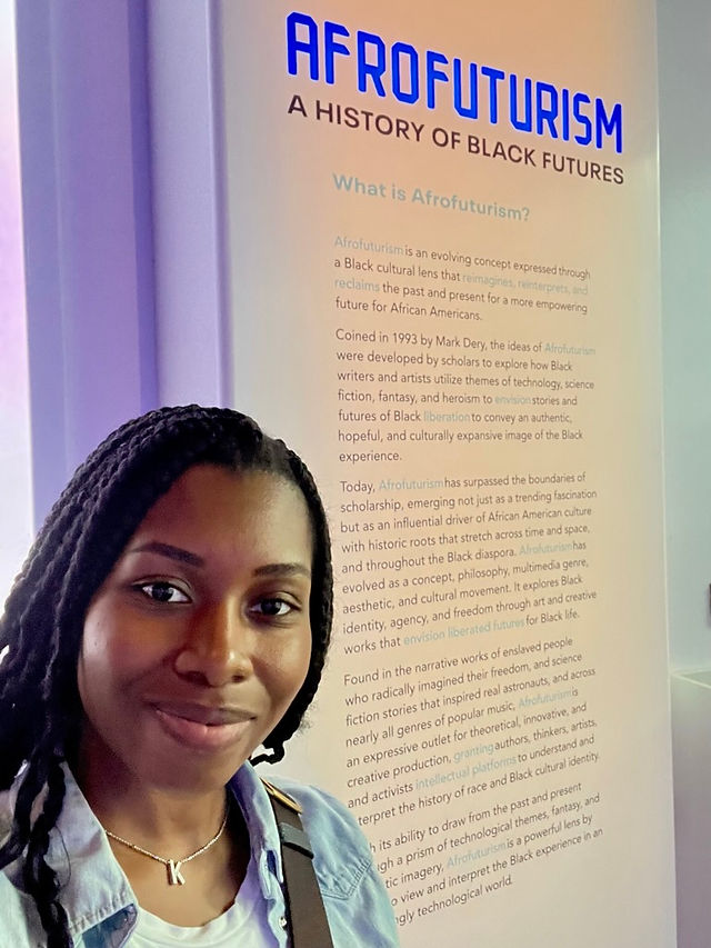 History of Afrofuturism large overview placard with Kimi taking a selfie with it 