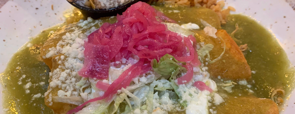 3 chicken enchiladas in green sauce with a cup of refried bean topped with 2 tortilla chips and a side of rice.