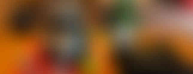 Margarita Prep Bench featuring a blender, margarita glass, handheld citrus juicer, and a jigger are on the left. On the right is a bottle of orange liqueur, and a black apron with The Mayan Cacao Company logo on the front with a white chef's hat underneath the folded apron.