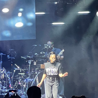 Janet Jackson Final Act. She's wearing a black Rhythm Nation crop top, black baggy wide leg jeans with a belt and her now signature high ponytail.