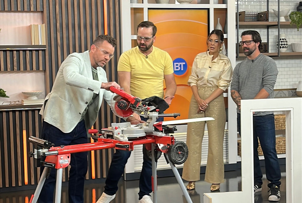 Four people in a studio watch as one uses a red miter saw on wood. Background has shelves and an orange BT sign. Curious mood.