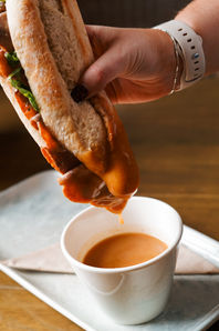 Rare roast beef baguette being dunked into a peppercorn sauce