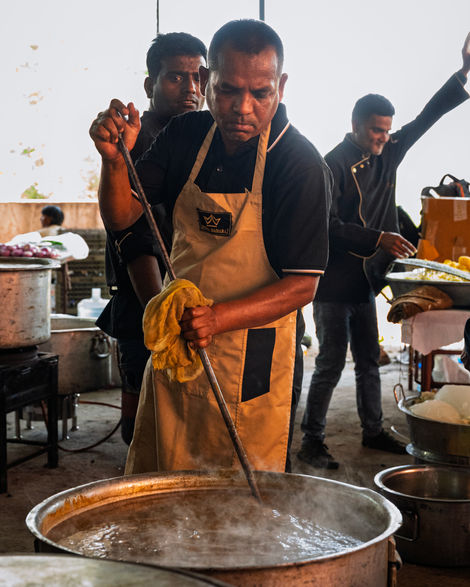Man stirring large pot at outdoor cooking event.