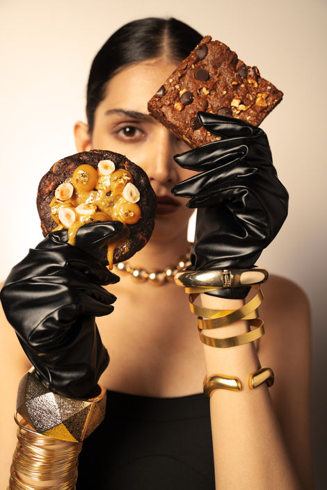 Woman holding cookies, wearing black gloves and jewelry.