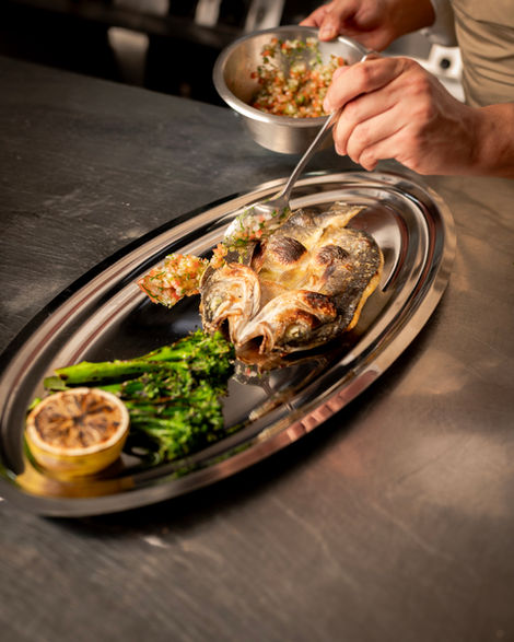 Person preparing fish dish with vegetables and lemon.