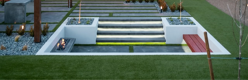 Modern garden with illuminated stone steps, a fire pit, red bench, and pebble landscaping on green grass. Minimalist and serene atmosphere.
