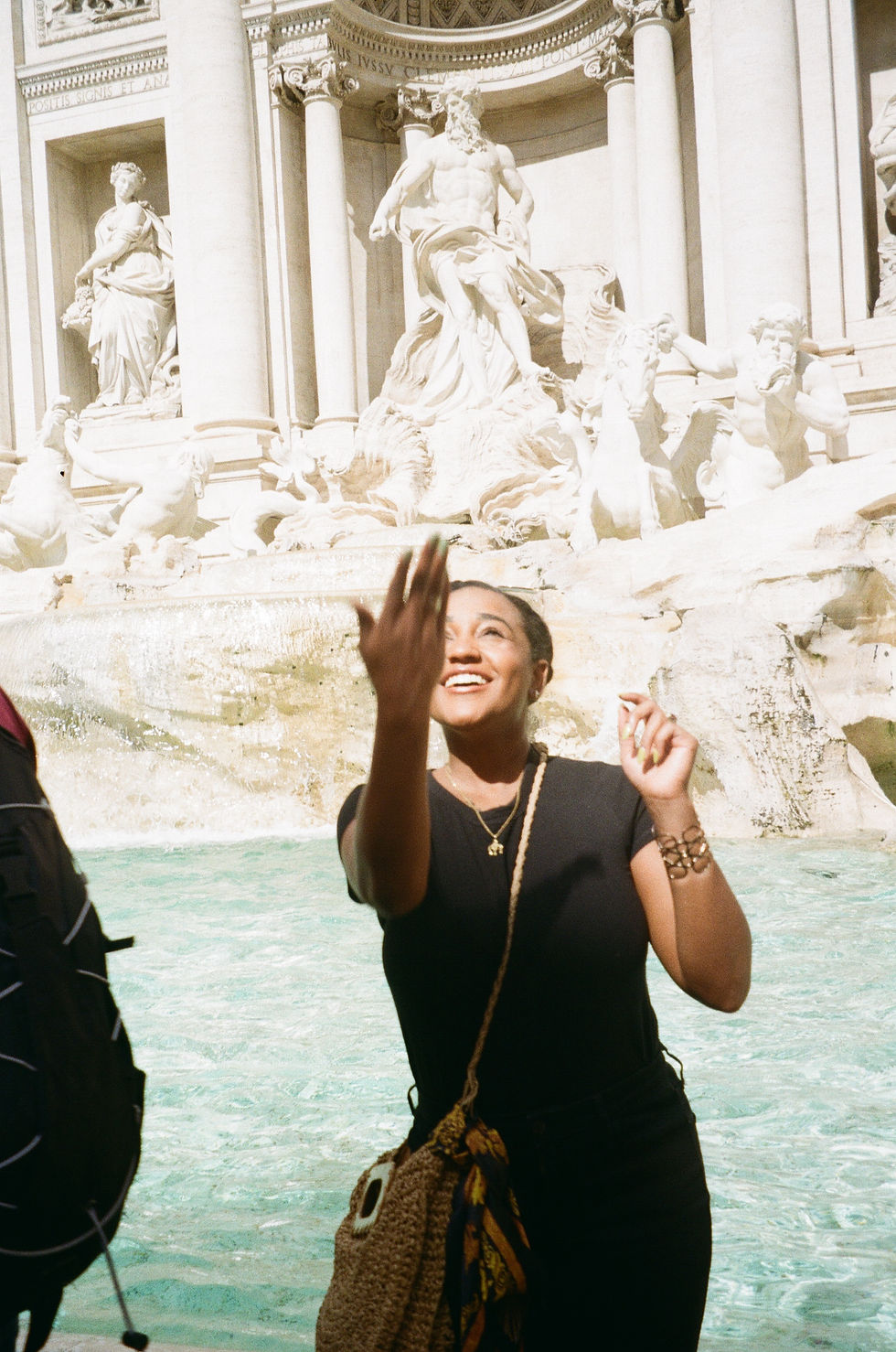 black woman traveler throwing a coin into the trevi fountain in rome italy