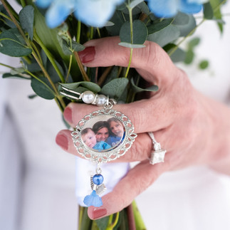 Elder bride holding a bouquet of flowers with brooch with image in the middle with family.