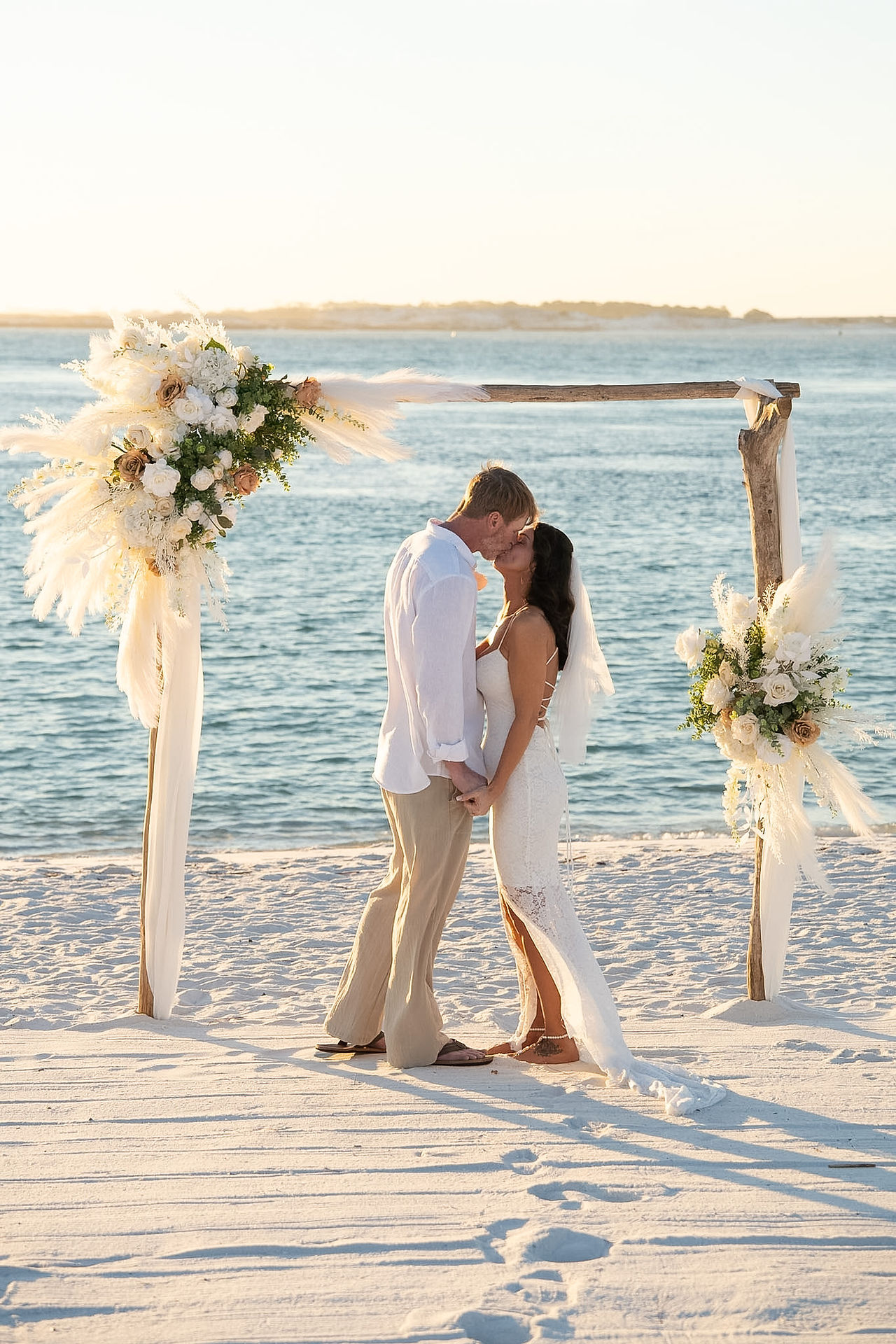Ceremony arbor with couple standing below it on the beach.