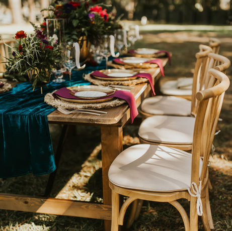 Outdoor wedding decor with rich colors of turquoise and red velvet with a table setting on the lush grass.