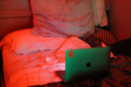 a photo of an unmade bed with an open laptop on it, lit with green and red lighting