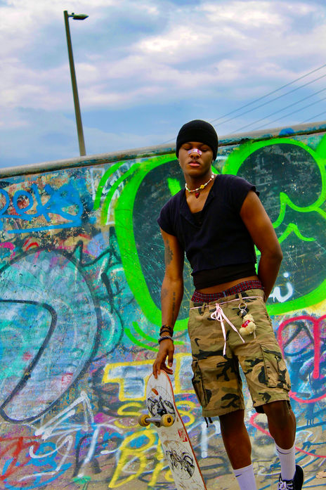 a person standing in the bowl of the skate park. He has dark skin and is holding a skate board