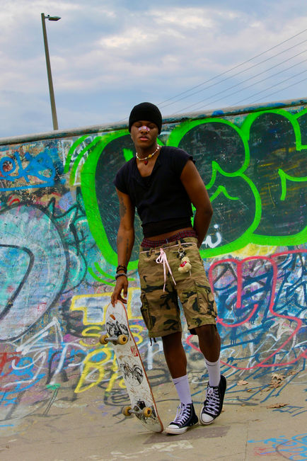 a person standing in the bowl of the skate park. He has dark skin and is holding a skate board