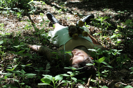A photo of a person with makeup to look like they're decaying and illustrations of eyes covering them, laid on the forest floor