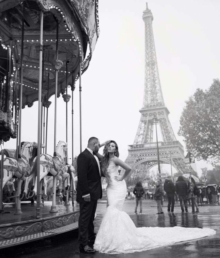 Bride and groom pose near a carousel in Paris, with the Eiffel Tower in the background. The scene is elegant and romantic in black and white.