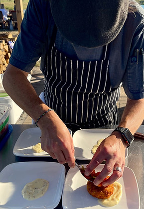 A picture of the chef at Field Trip Kitchen preparing food at a farm to table dinner. He is putting food on a plate as he leans over.