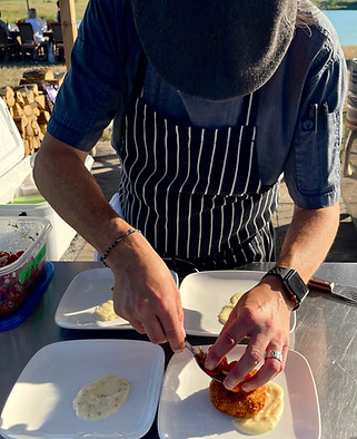 A picture of the chef at Field Trip Kitchen preparing food at a farm to table dinner. He is putting food on a plate as he leans over.