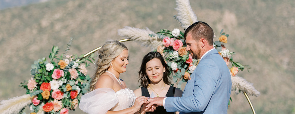 Bride and groom standing beneath a floral gold ceremony arch with saguaro cactus views