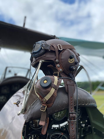 A brown flight hat and goggles resting on the cockpit of a plane