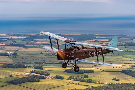 A Tiger Moth plane flying over the Northumberland landscape