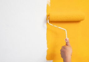 A left hand is rolling a line of bright yellow paint with a roller.
