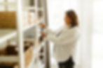 Women in white shirt, with brown hair, standing infront of a book case, organzing