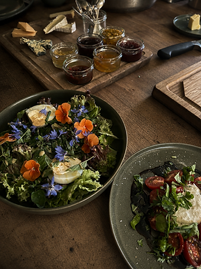 Sallad med ätbara blommor intill charkuterier och tillbehör.