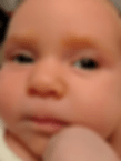 Close-up of a baby's face with a neutral expression. The baby's skin is smooth and rosy, with a light background.