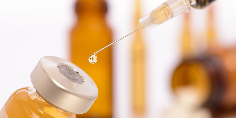 Syringe needle with droplet above a vial. Amber bottles in blurred background. Focus on clear liquid in needle tip, evoking precision.