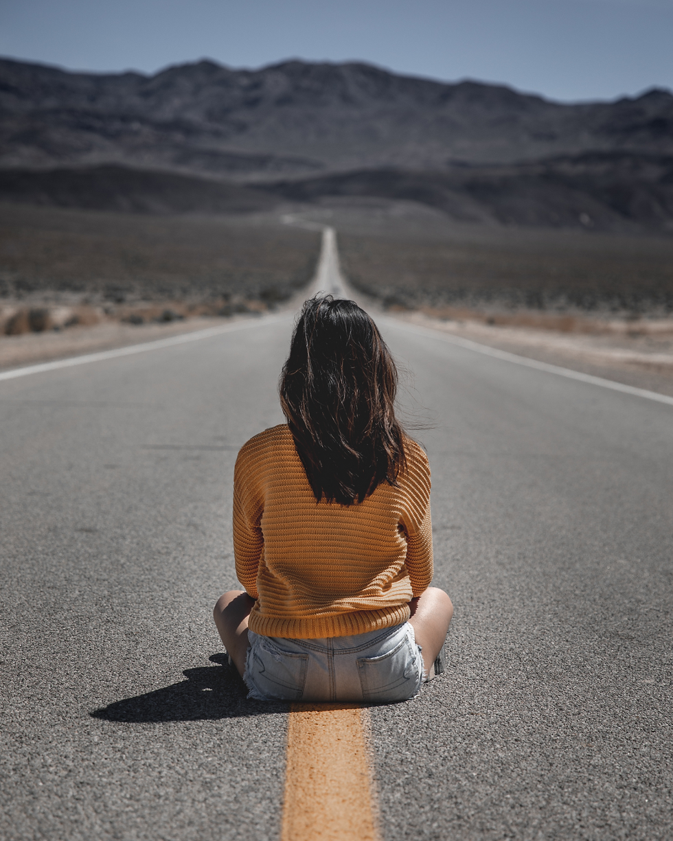 Mulher sentada no meio de uma rodovia vazia encarando a travessia.
