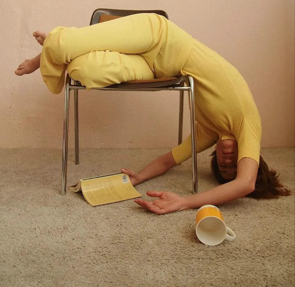 Mulher de amarelo caída sobre uma cadeira como que aparentando sem vontade pra fazer sua leitura.