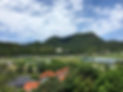 島根県隠岐の島。白い雲が浮かぶ青い空。都万地区にある高田山を背景に、赤と黒の瓦屋根、緑の田園が見える風景。