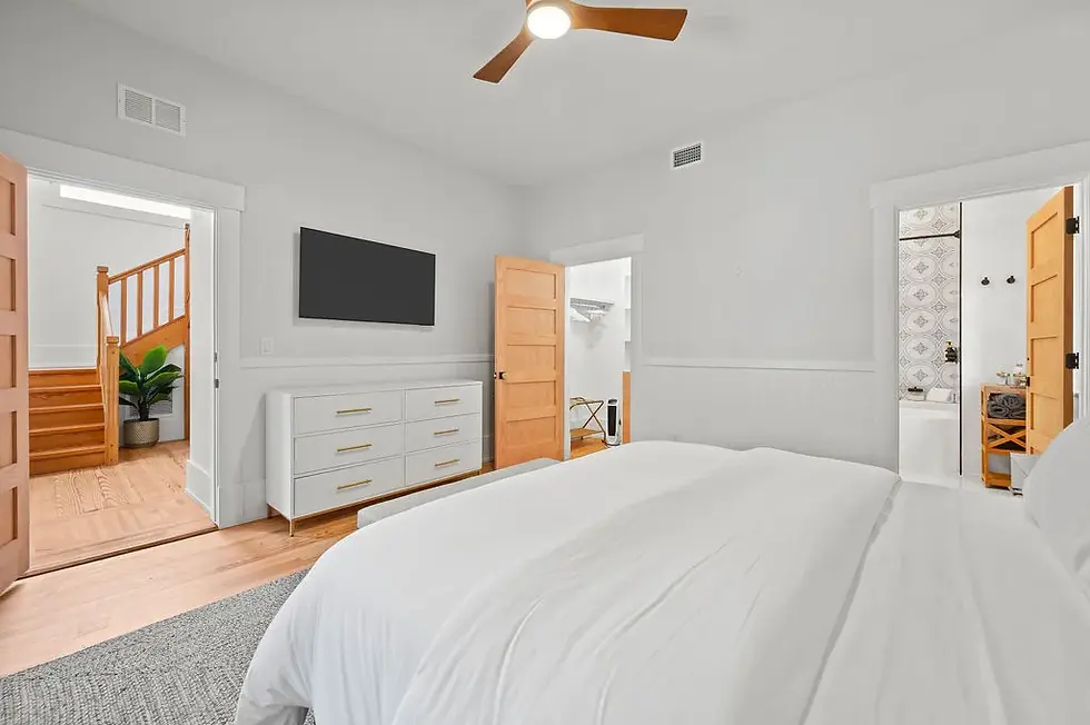 Modern primary bedroom in luxury short term rental St Augustine featuring white bed, wood accents, and ensuite bathroom