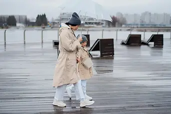 Woman holding an umbrella over a child dressed identically to her, symbolizing protection and healing of her inner child