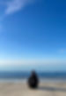lucille gastineau assise en tailleur sur la plage, elle est de dos et face à la mer