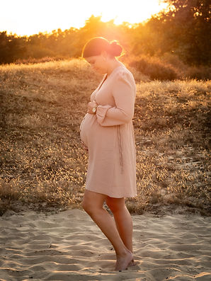 Schwangere Frau steht in Seitenansicht im Licht des Sonnenuntergangs