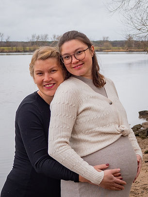 Zwei schwangere Frauen stehen hintereinander dicht zusammen und umfassen den Bauch der vorderen Frau